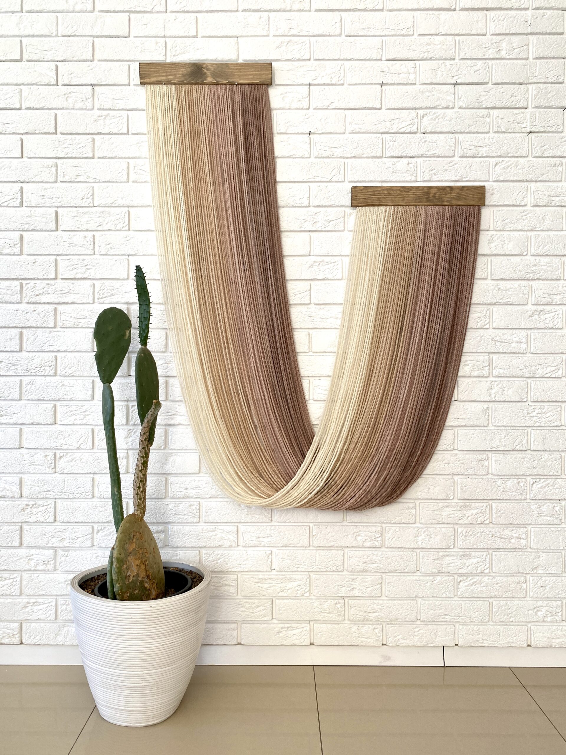 pastel wool decoration hanging on the wall with a flower standing next