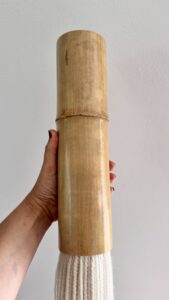 Close-up of a handmade bamboo wall hanging showing the natural bamboo tube and thick cream wool fibers, highlighting the organic texture and craftsmanship.