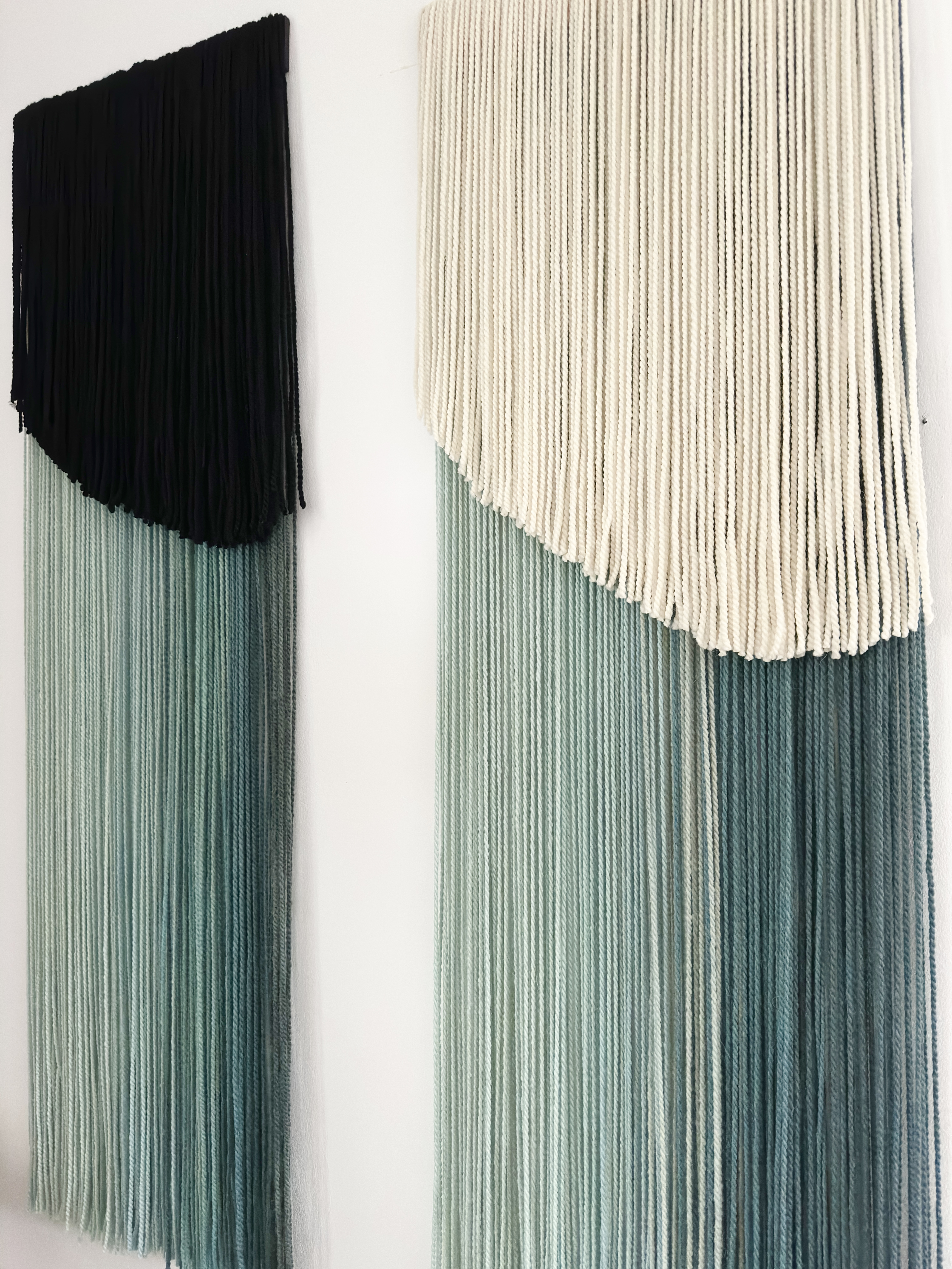 Set of two handmade wall hangings crafted from hand-dyed merino and sheep wool in green and cream tones.