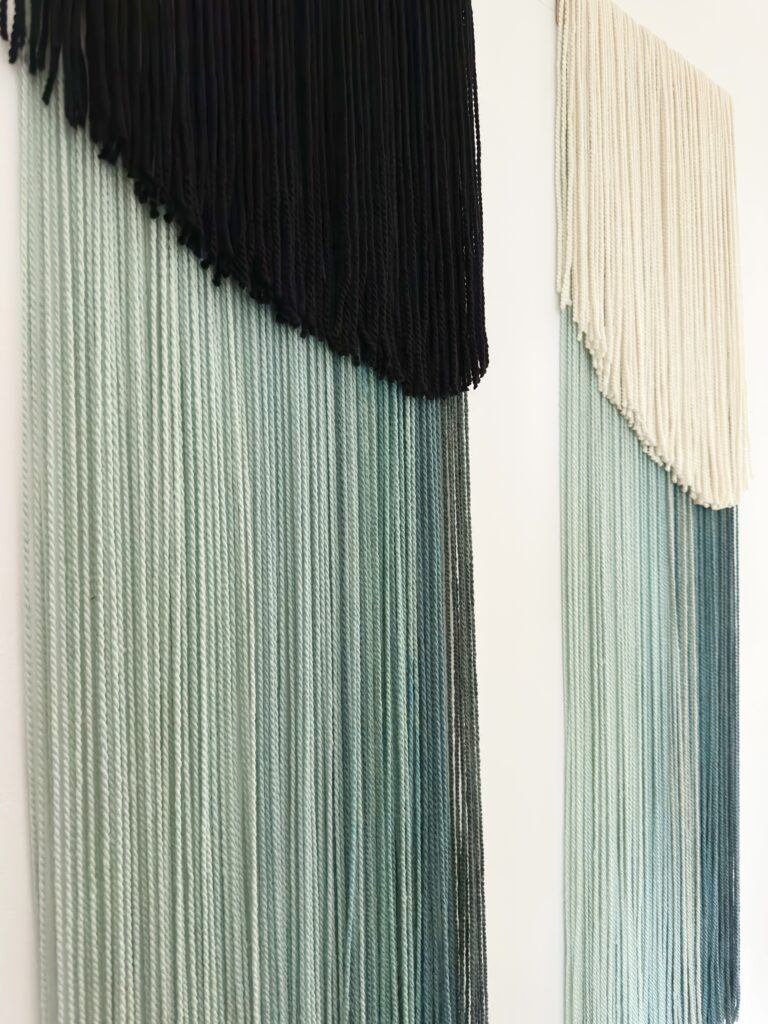 Set of two handmade wall hangings crafted from hand-dyed merino and sheep wool in green and cream tones.