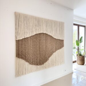 Large handwoven wool and jute wall hanging by Olivia Fiber Art displayed in a bright interior with a plant, highlighting natural textures and organic design.